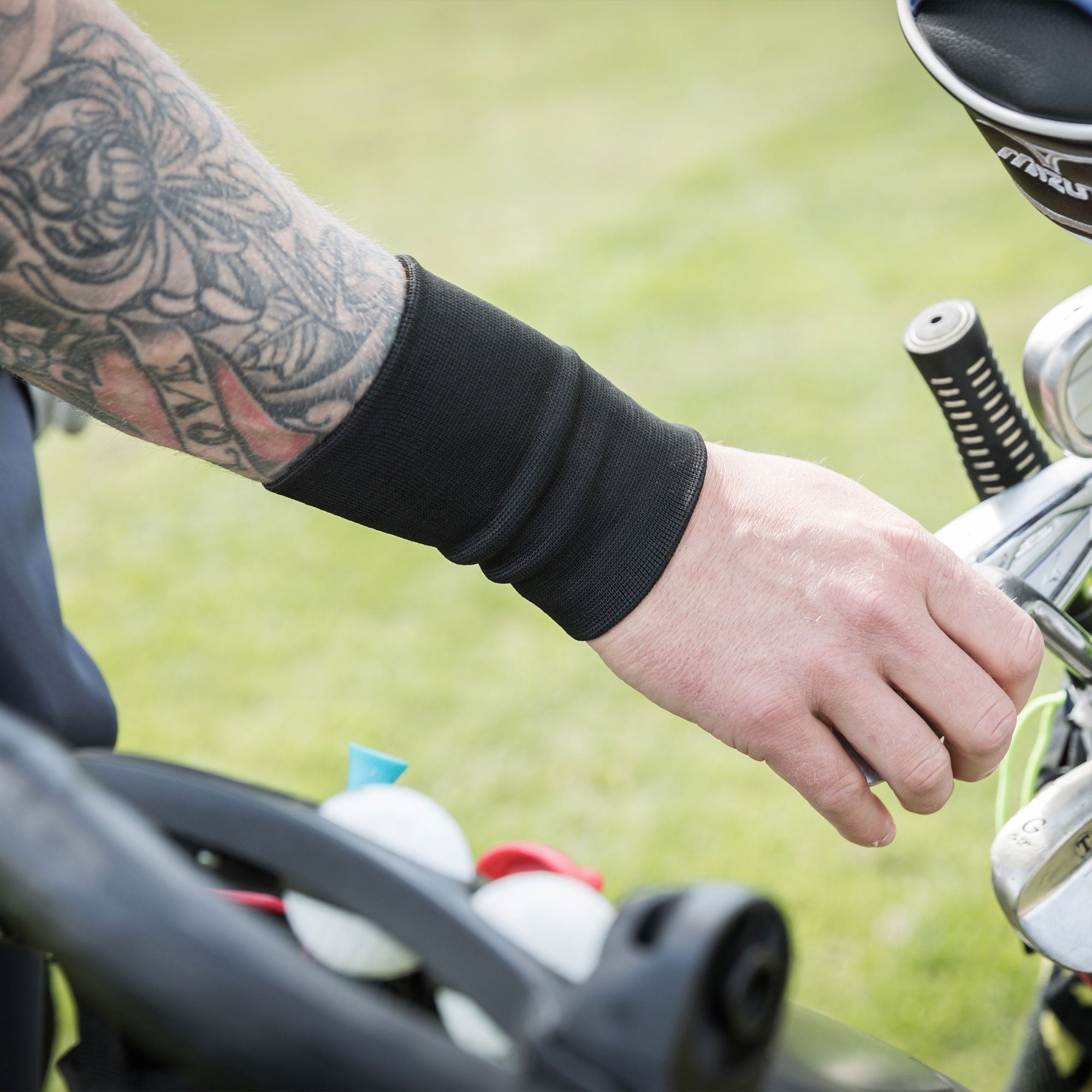 Handgelenkschoner 1300 am tätowierten Arm neben Golfausrüstung